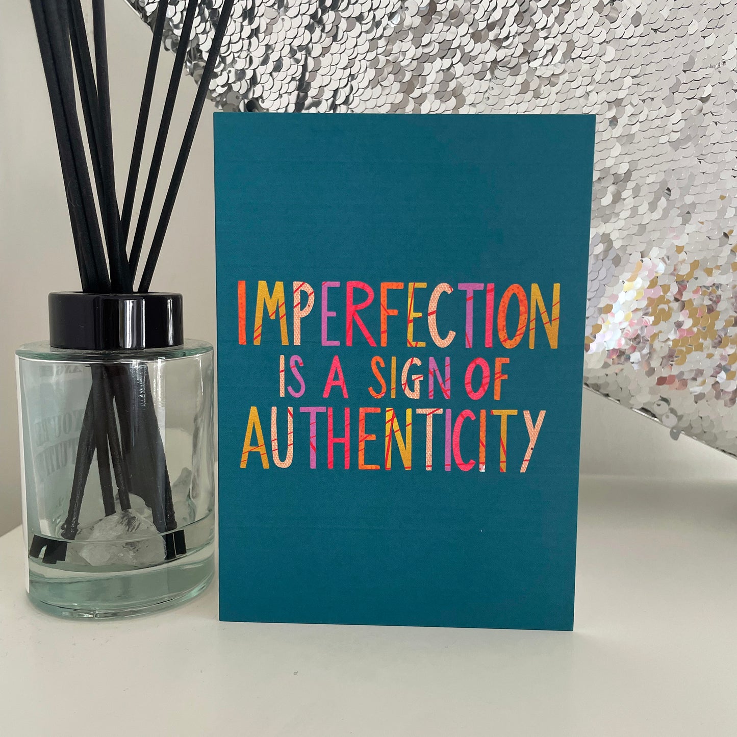 Image shows a teal coloured greetings card with the wording 'Imperfection is a sign of authenticity'