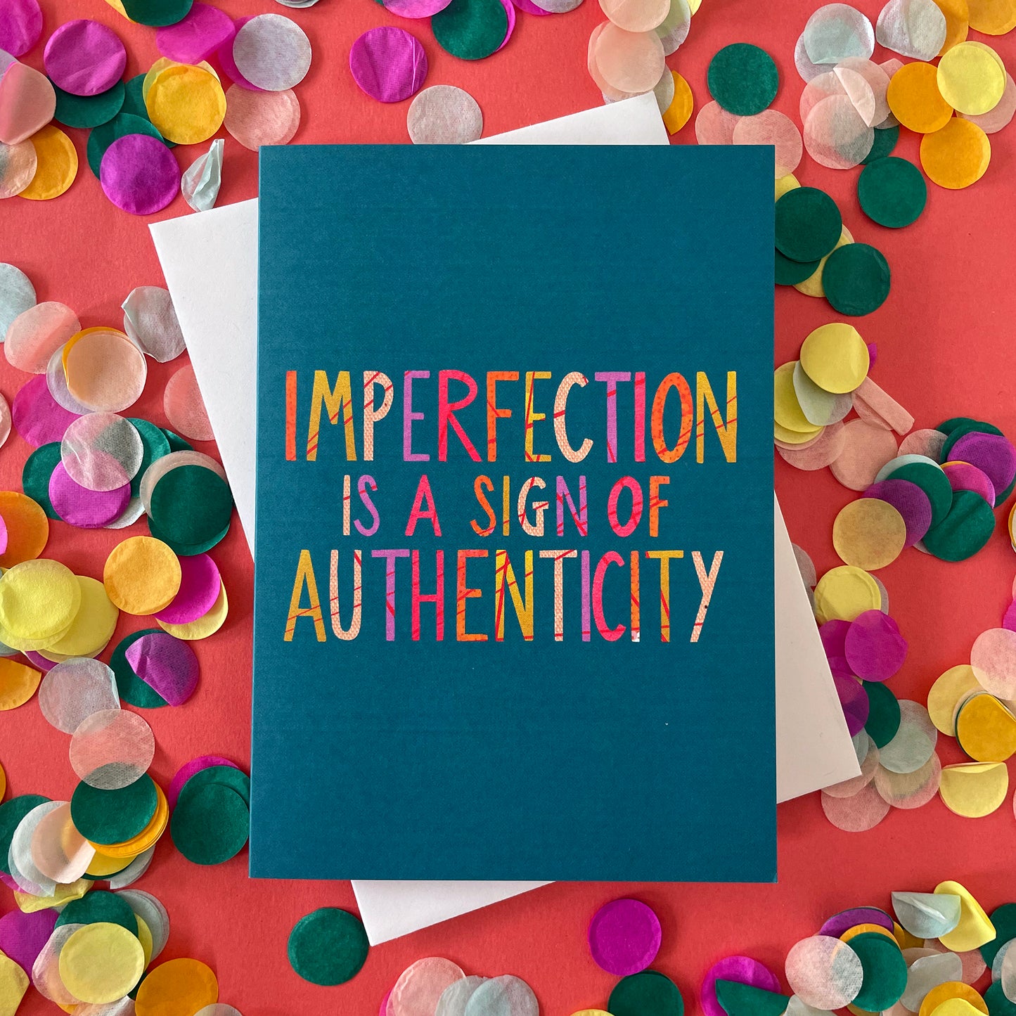 Image shows a teal coloured greetings card with brightly coloured wording that reads 'Imperfection is a sign of authenticity'