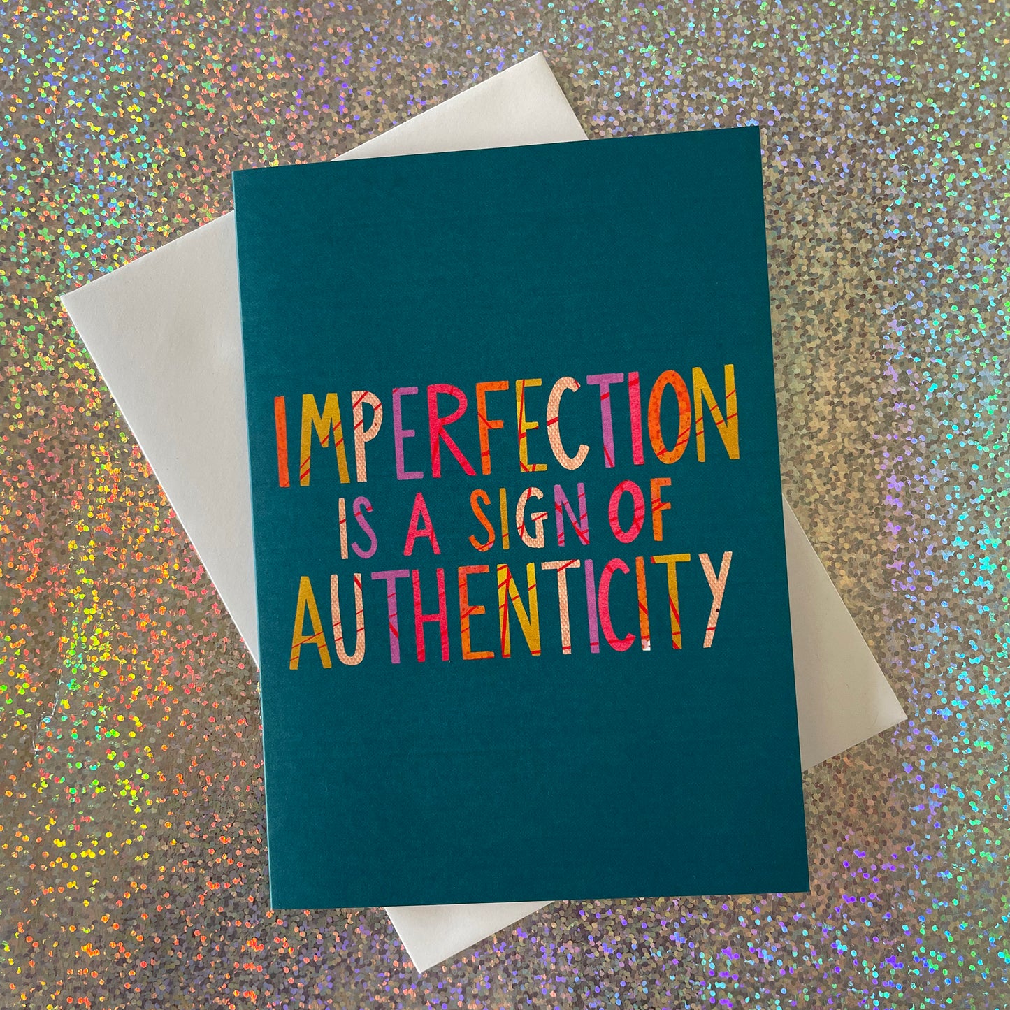 Image shows a teal coloured greetings card with the wording 'Imperfection is a sign of authenticity'