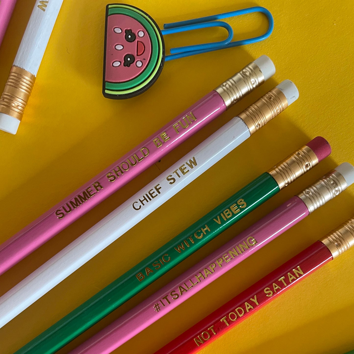 Image shows a collection of pencils including pink pencil with gold lettering that says #itsallhappening, a pink one that says summer should be fun, a white one that says chief stew, a green one that says basic witch vibes and a red one that says not today satan.