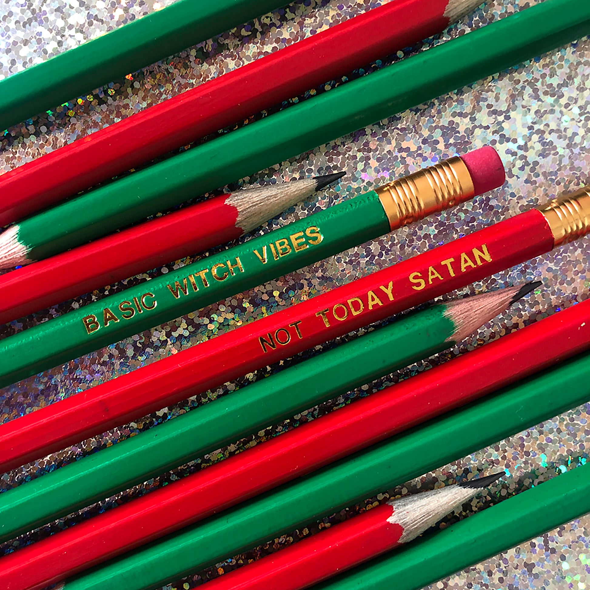 Image of a collection of pencils in bright red and green The red pencils are embossed in gold with 'not today satan' and the green ones are embossed in gold lettering with 'basic witch vibes'