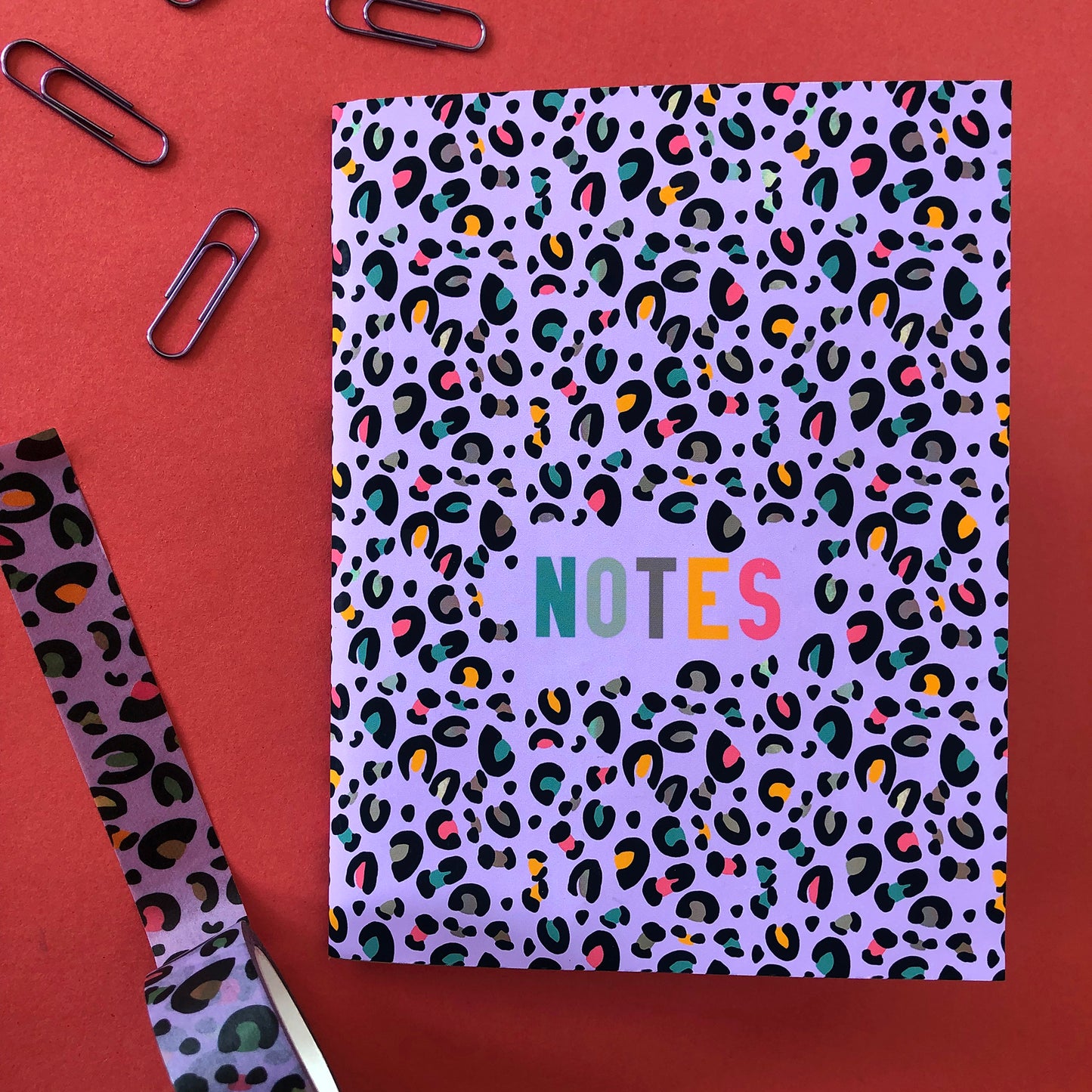 Image shows an A6 notebook in a bright purple with a leopard print pattern featuring pops of neon