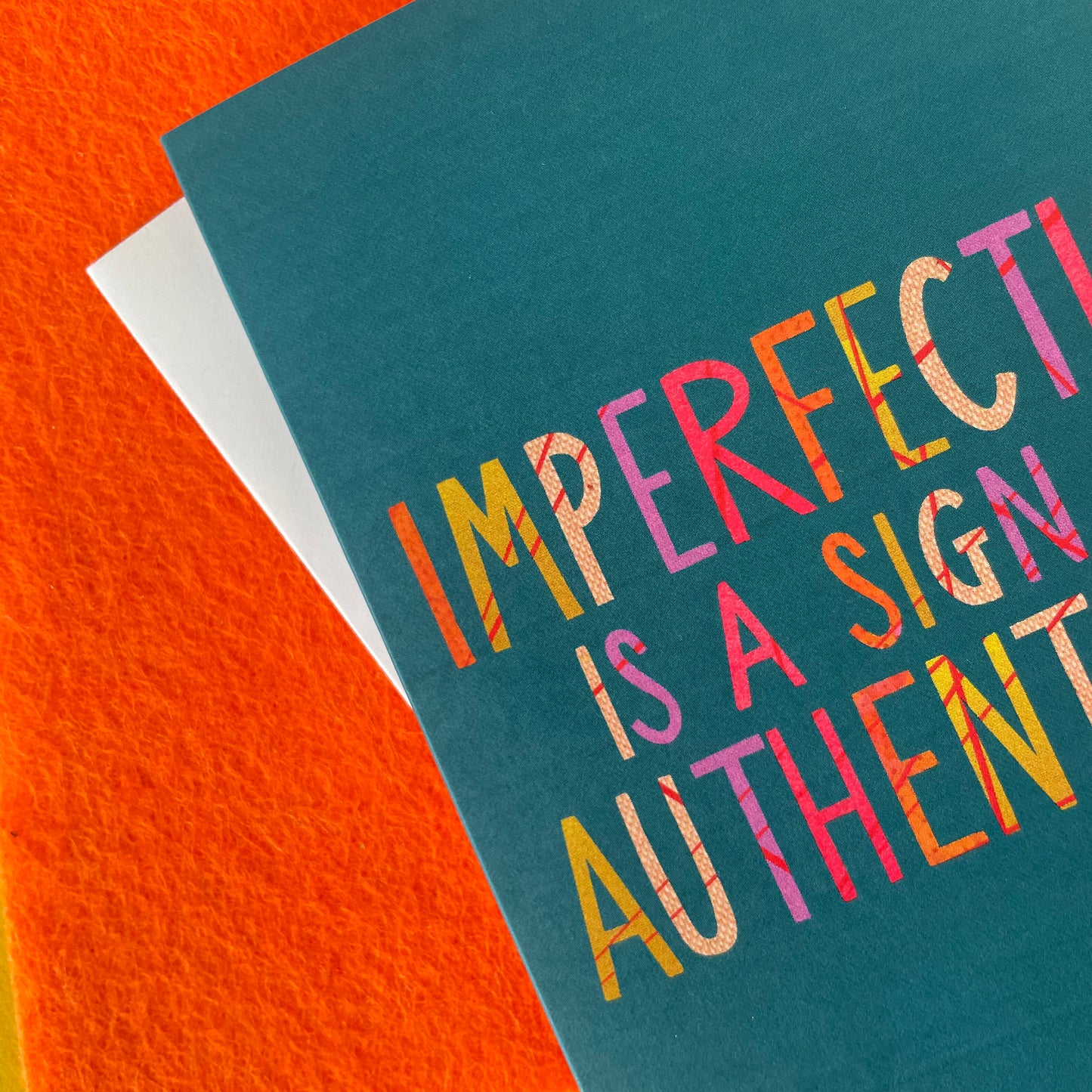 Image shows a teal coloured greetings card with the wording 'Imperfection is a sign of authenticity'