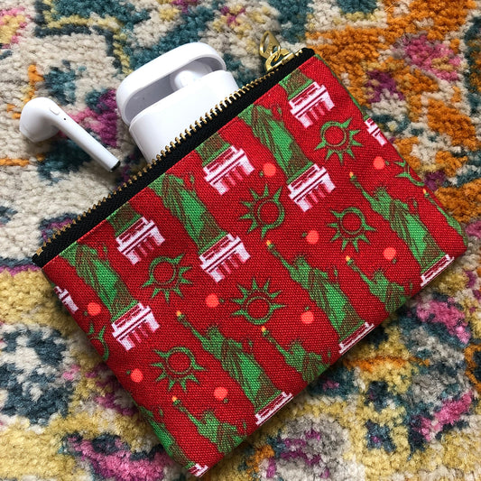 Image shows a handy zip pouch in a bold red colour with a statue of liberty pattern in green and white.