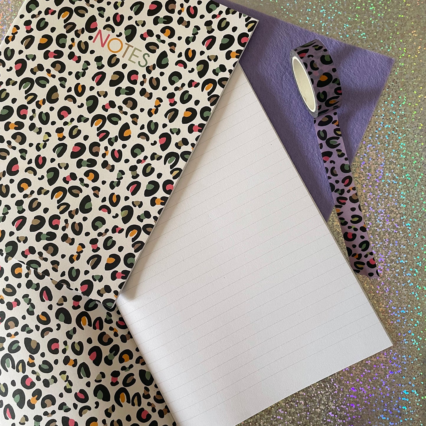 Image of a leopard print A5 size notebook in a cream colour with pops of neon. Image also shows the notebook open with lined pages and a leopard print inside cover.