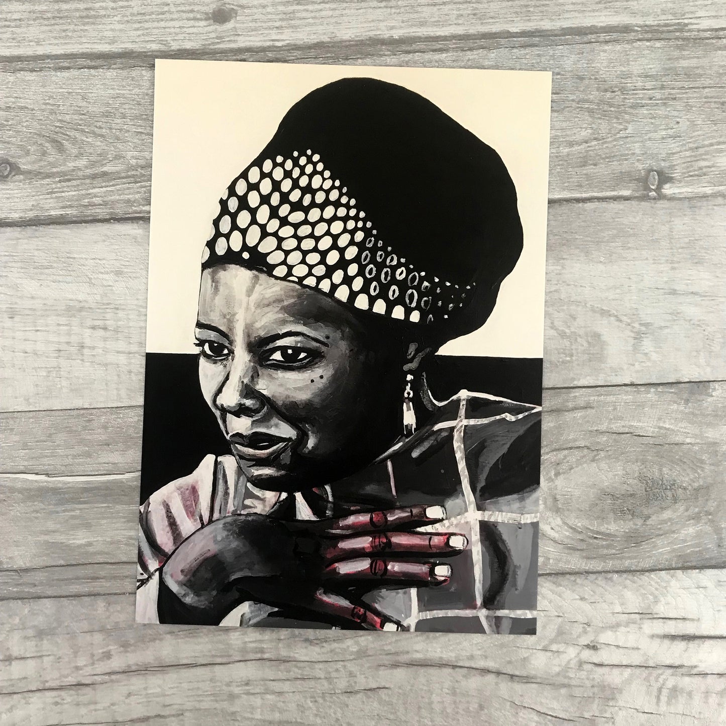 Image shows a framed black and white portrait of Maya Angelou. Artwork is painted in black and white wirth a pink undertone visible in the hand and shoulder