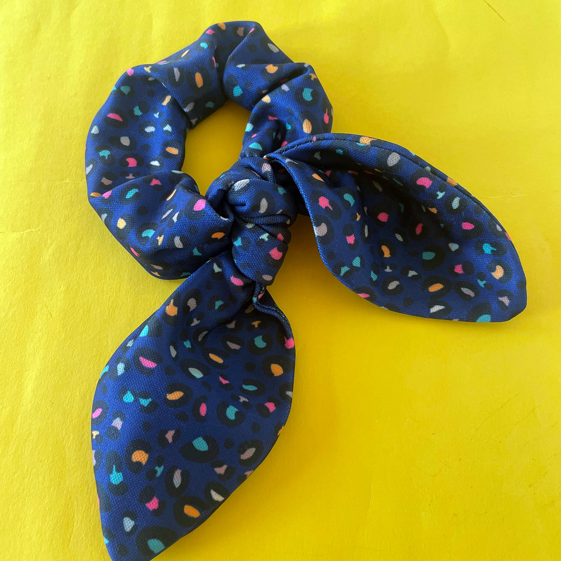 Image shows a handmade midnight blue leopard print hair scrunchie with a bow.