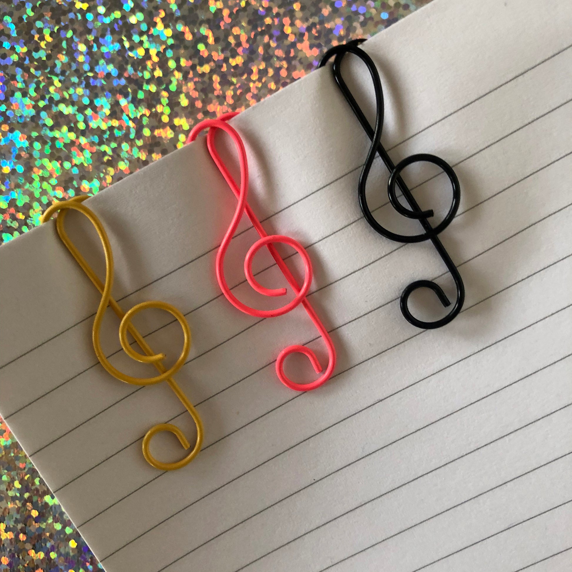Image shows a set of pink, black and gold, treble clef shaped paperclips.