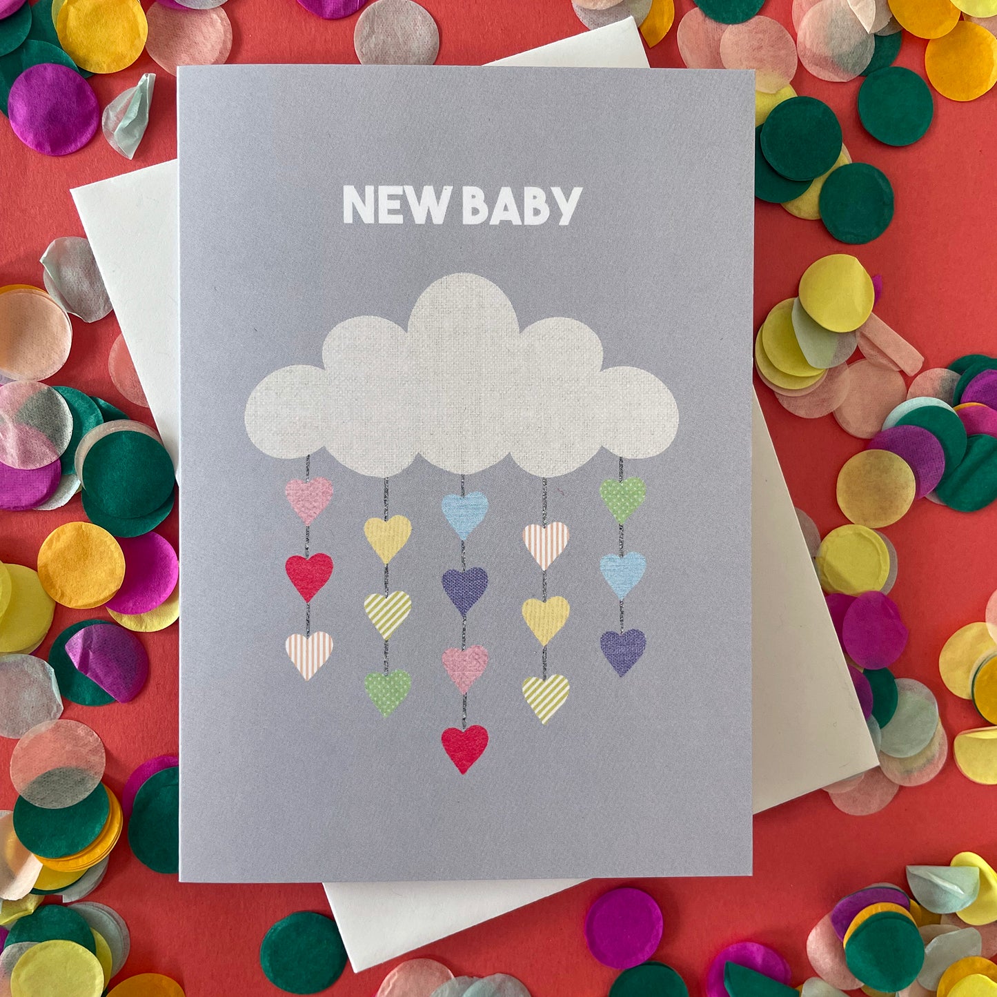 Image shows a pale grey greetings card with an illustration of a cloud with colourful hearts hanging from it and the words 'New Baby'