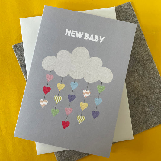 Image shows a pale grey greetings card with an illustration of a cloud with colourful hearts hanging from it and the words 'New Baby'