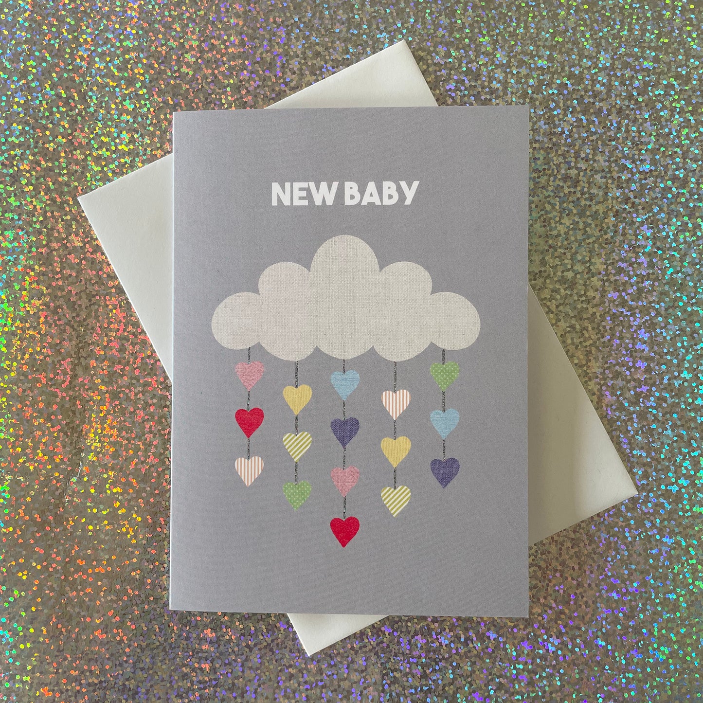 Image shows a pale grey greetings card with an illustration of a cloud with colourful hearts hanging from it and the words 'New Baby'