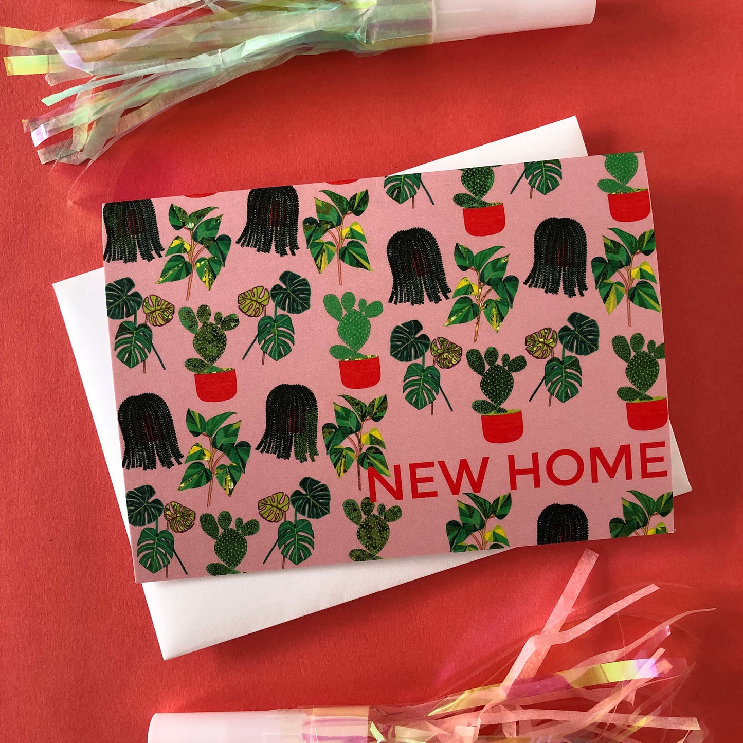 Image shows a pastel pink new home card with a pattern of illustrated green house plants and orange pots and writing.