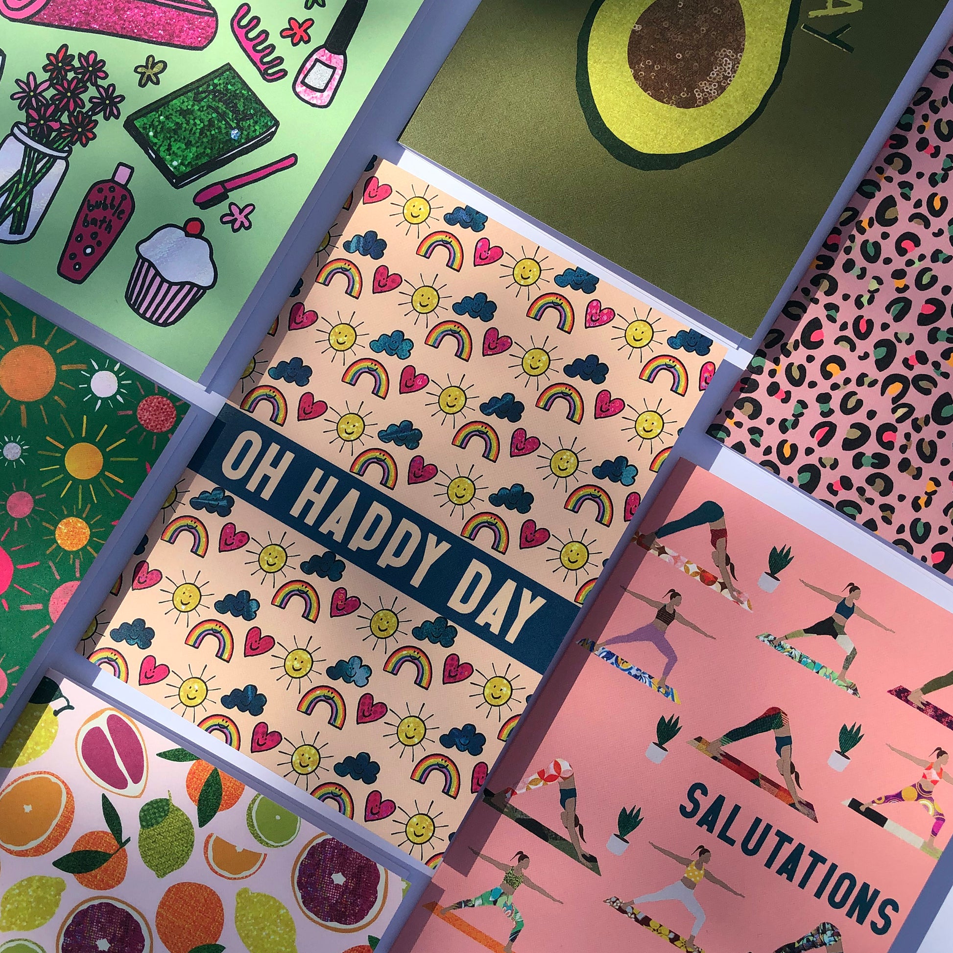 Image shows an everyday greetings card that says 'oh happy day' and features a fun pattern of suns, clouds and rainbows