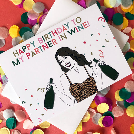 Image shows a fun and fabulous white birthday card with an illustration of a woman in a leopard print top holding 2 bottles of wine and the wording 'Happy Birthday to my partner in wine'..