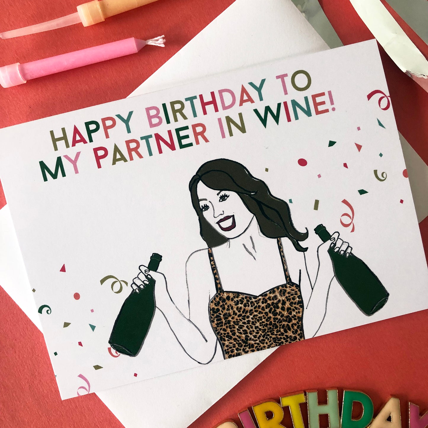 Image shows a fun and fabulous white birthday card with an illustration of a woman in a leopard print top holding 2 bottles of wine and the wording 'Happy Birthday to my partner in wine'..