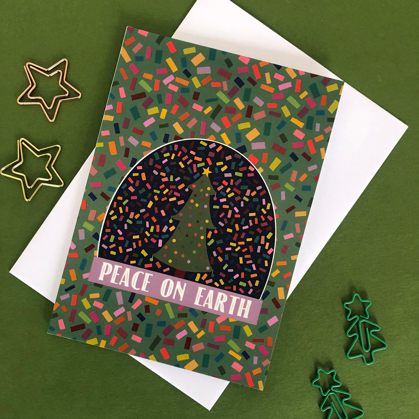 Image shows a bright and colourful Christmas card featuring an illustration of a snow globe on a confetti patterned background.