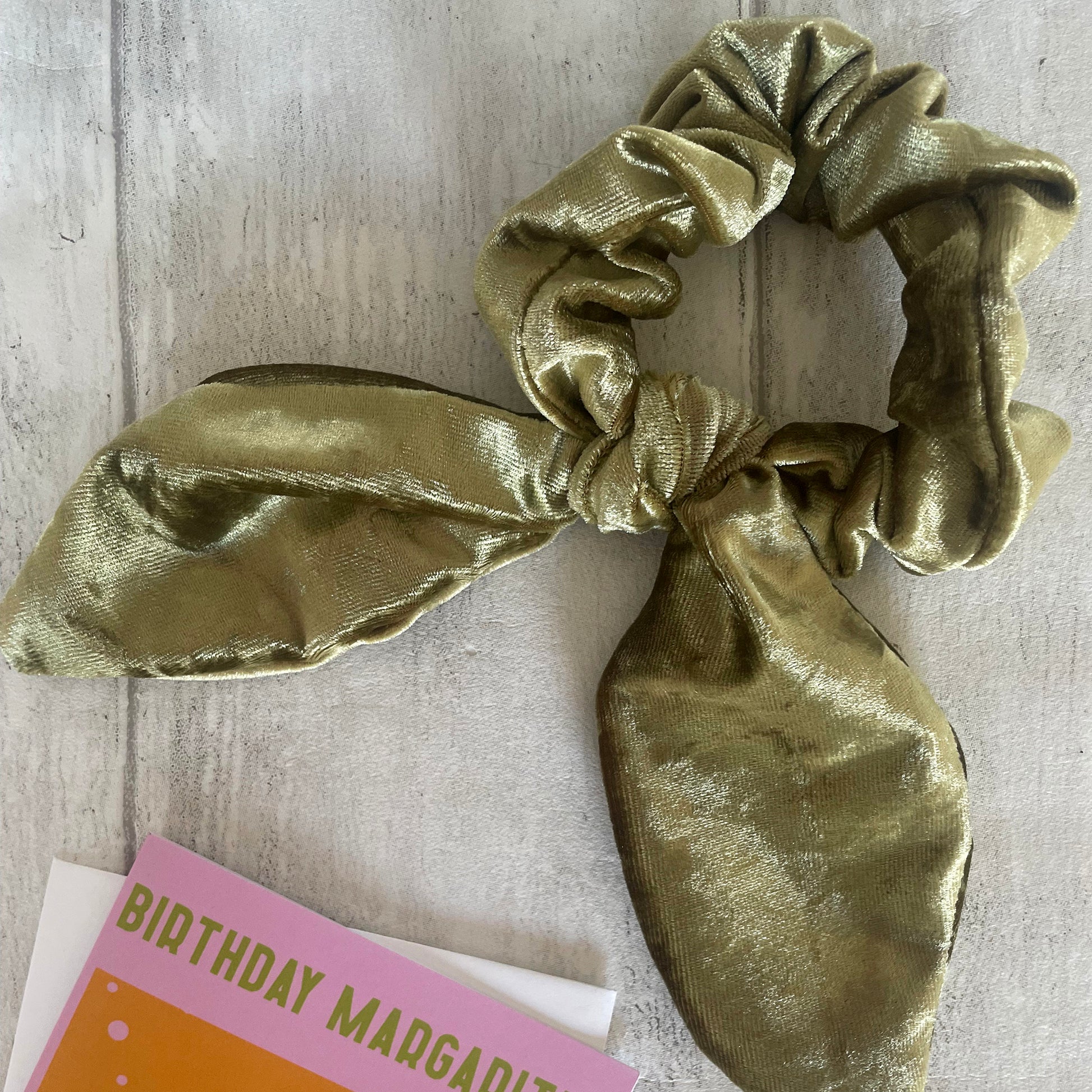 Image shows a peridot green velvet hair scrunchie with a knot and bow