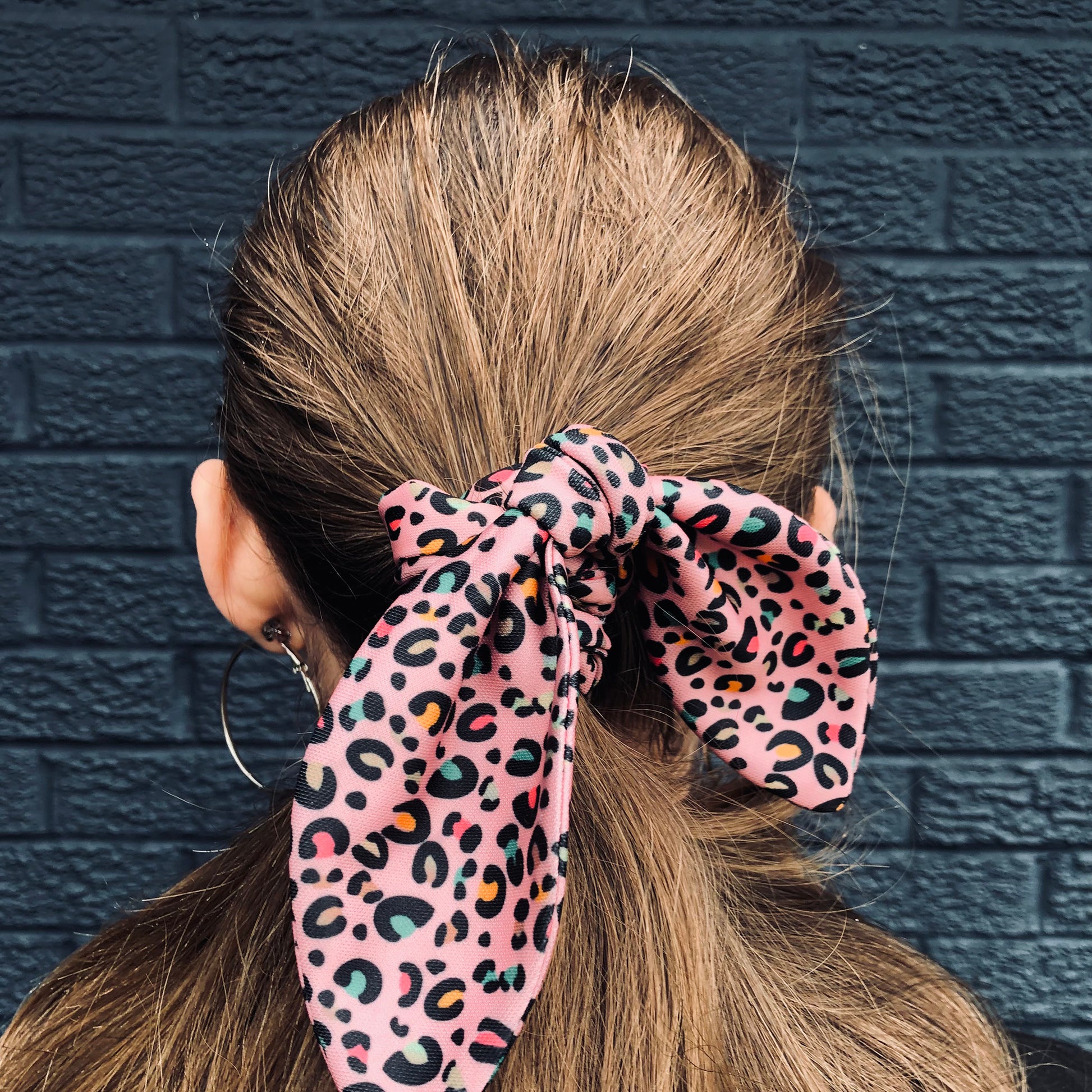 Image shows a pink leopard print hair scrunchie with a knot and bow