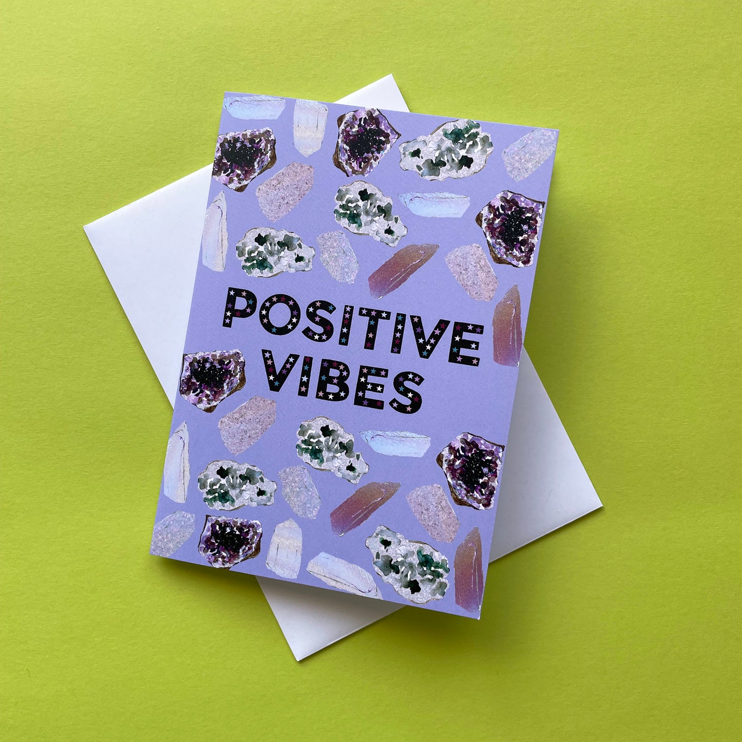 Image of a lavender coloured greetings card with illustrations of crystals and the words 'Positive Vibes'
