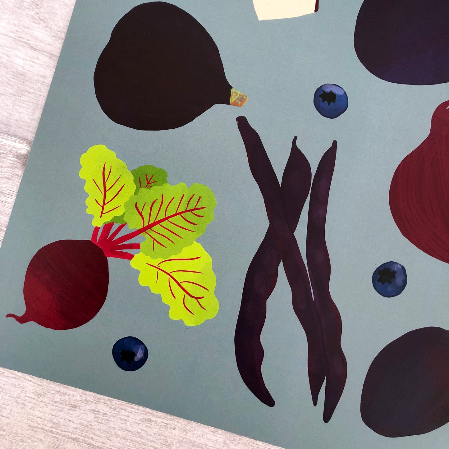 Close up image of an art print of purple fruit and vegetables on a pale indigo background.