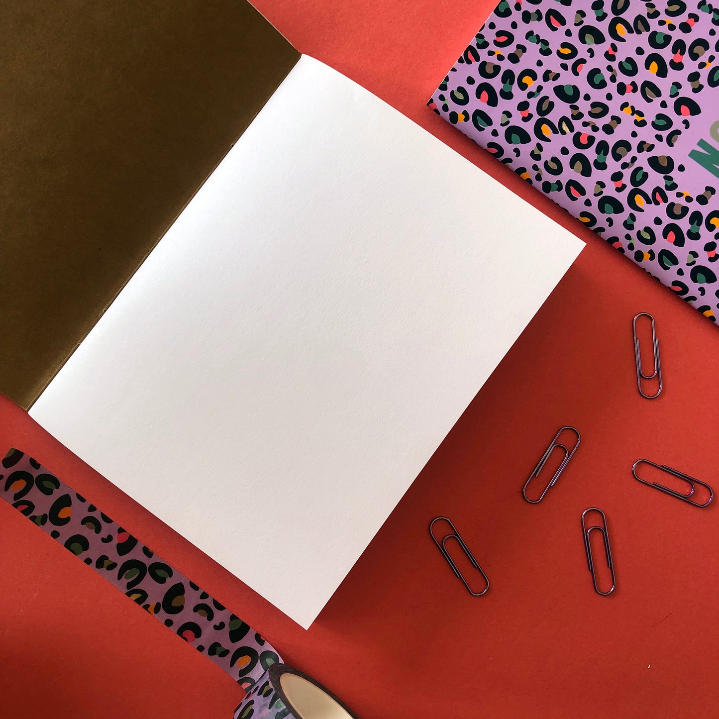 Image shows an open A6 notebook with blank white pages and a kraft inside cover. Also shown is a notebook front cover in a bright purple with a leopard print pattern featuring pops of neon
