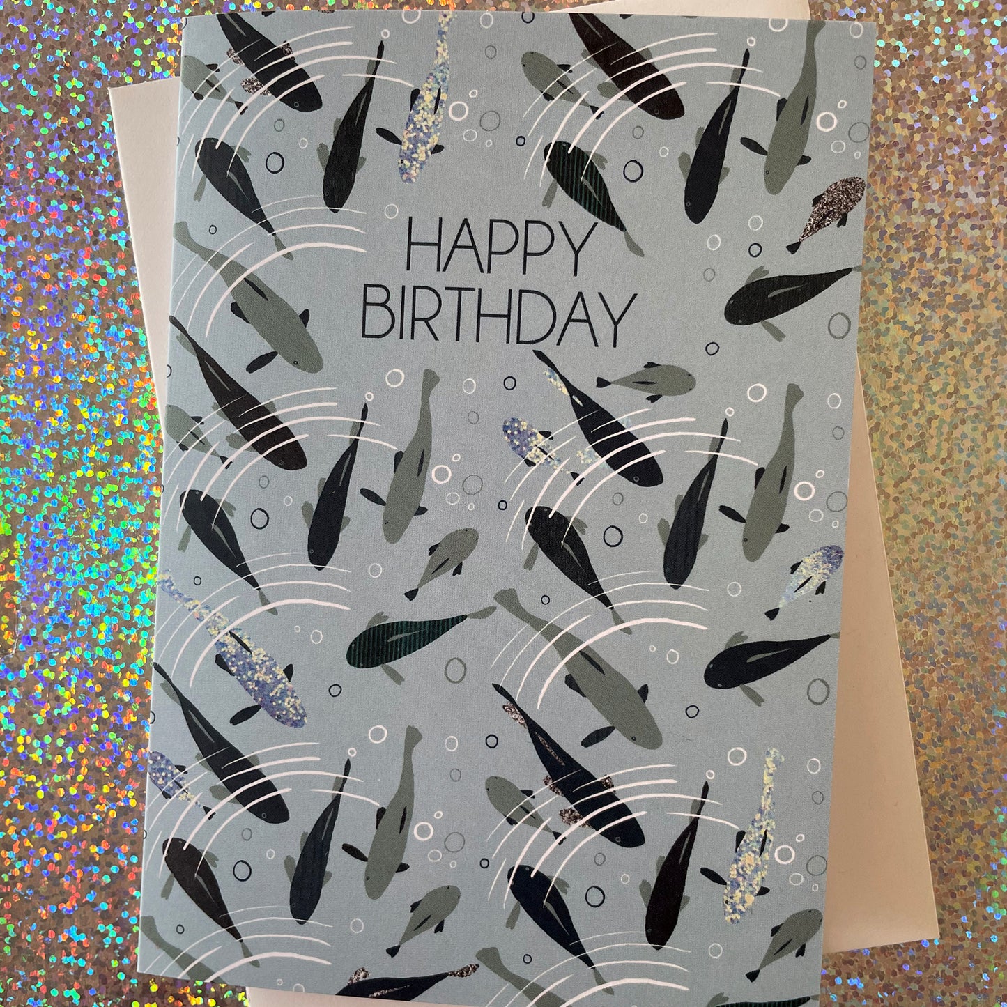 Image shows a pale blue birthday card with blue, silver and grey fish swimming under ripples of water and the words 'Happy Birthday"