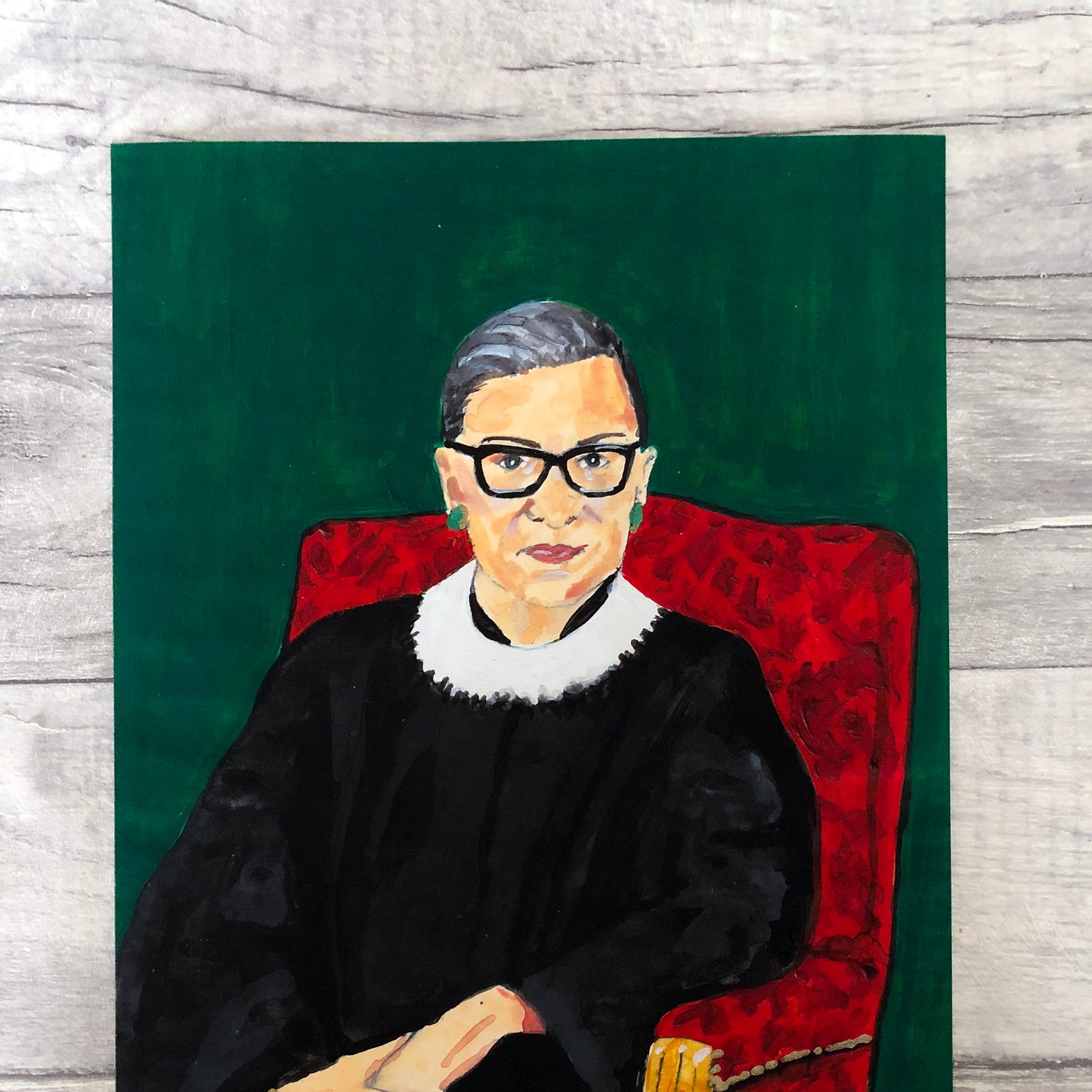 Image of a close up of art print of a portrait of Ruth Bader Ginsburg sitting on a red chair with a green background, originally painted in acrylics