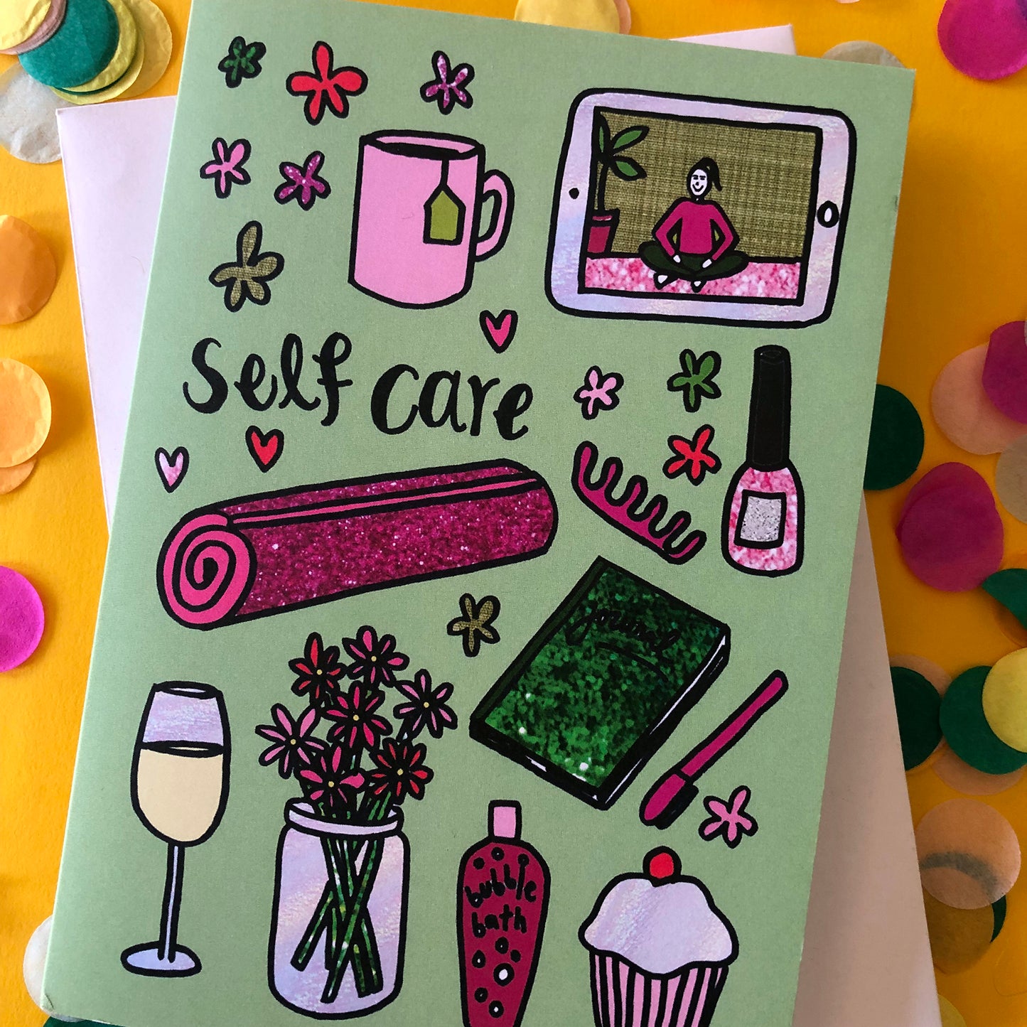 Image show a green greetings card that says 'self care' and features a fun pattern of self care items