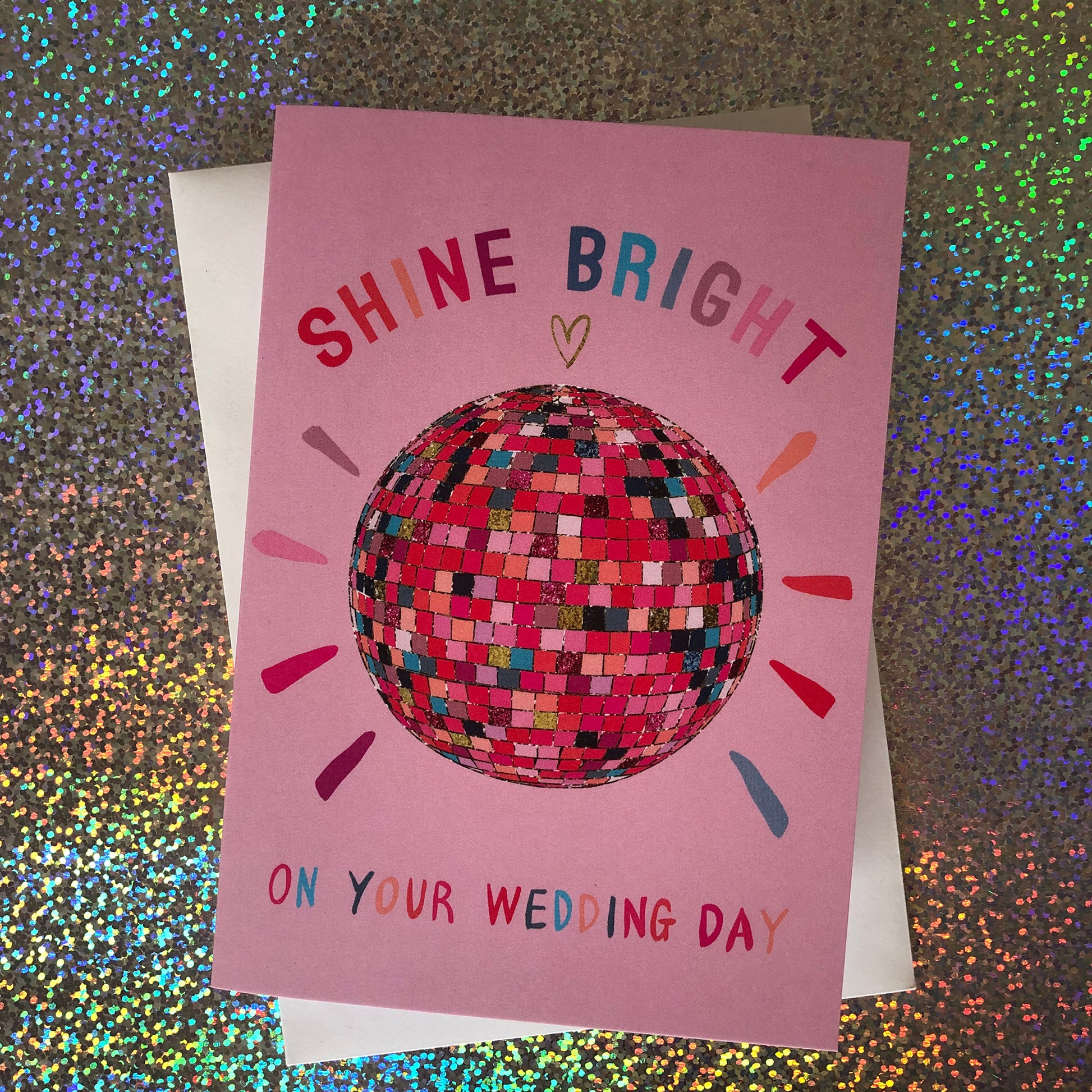 Image shows a pink wedding card featuring a glittery rainbow disco ball illustration and the words 'Shine Bright on your wedding day'.