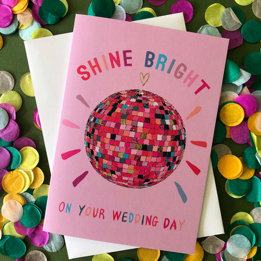 Image shows a pink wedding card featuring a glittery rainbow disco ball illustration and the words 'Shine Bright on your wedding day'.