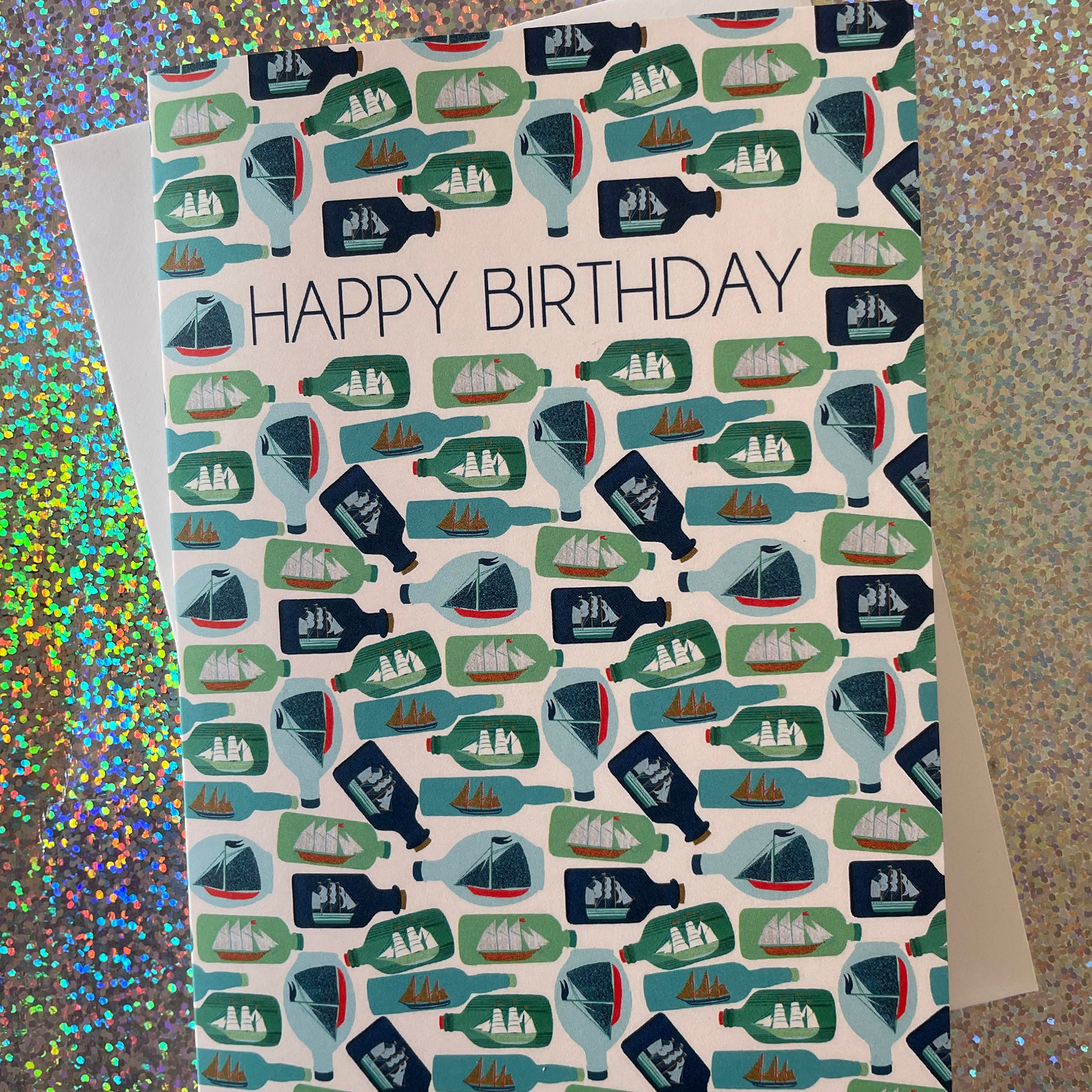 Image shows a birthday card with the greeting 'Happy Birthday' and an illustrated ships in bottles pattern.