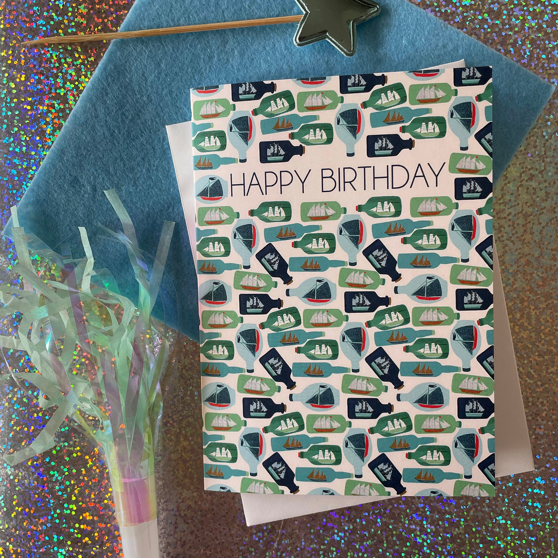 Image shows a birthday card with the greeting 'Happy Birthday' and an illustrated ships in bottles pattern.