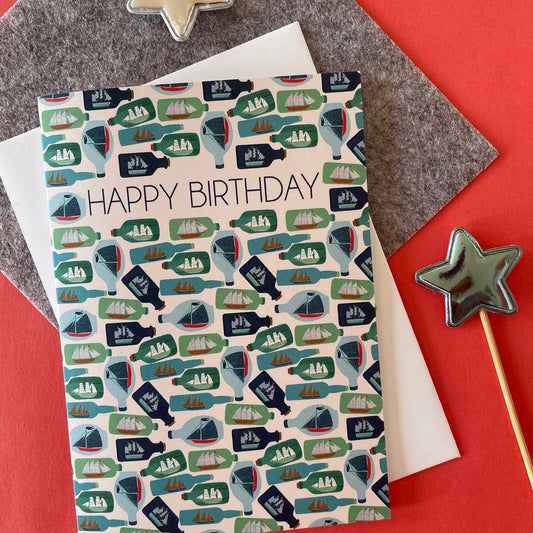 Image shows a birthday card with the greeting 'Happy Birthday' and an illustrated ships in bottles pattern.