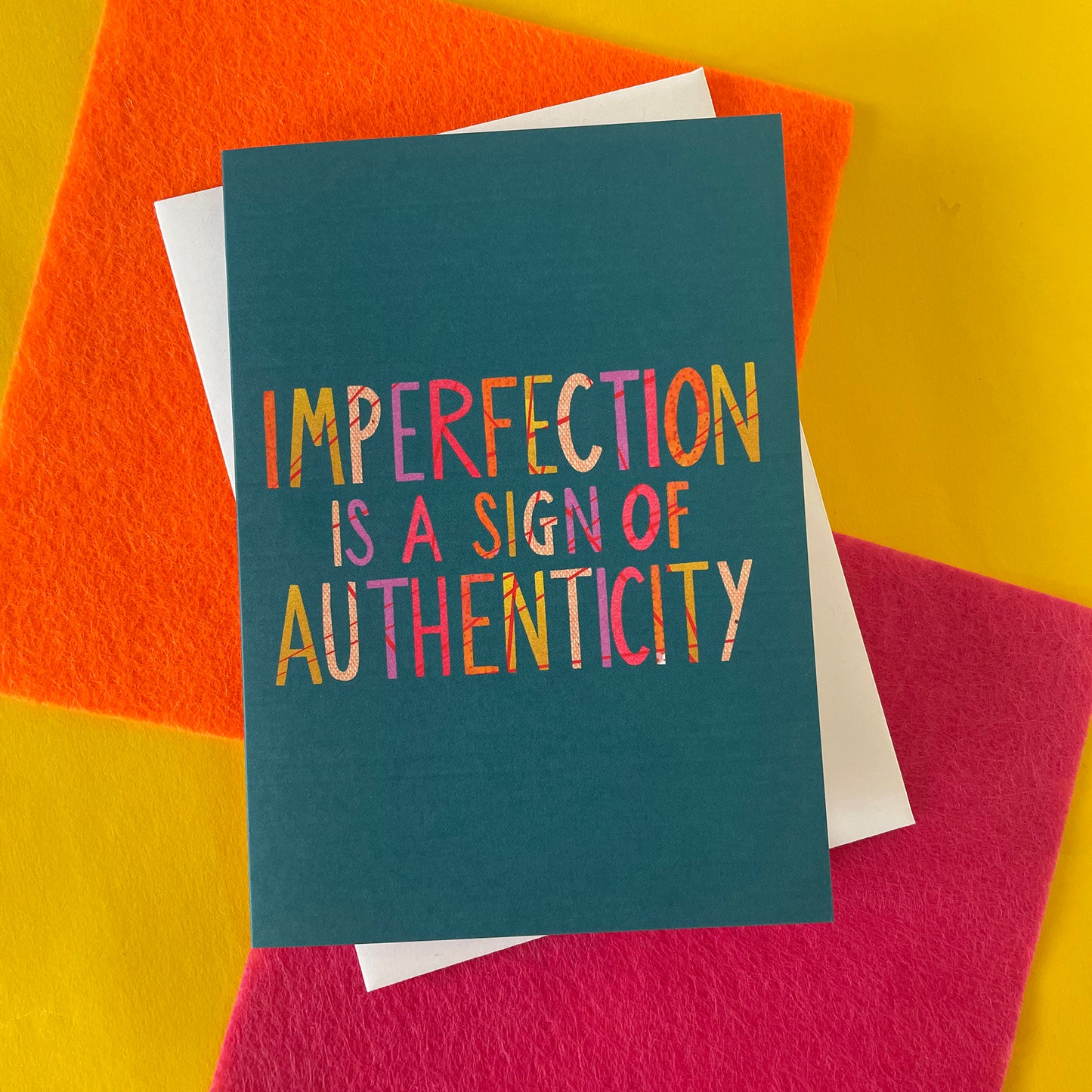 Image shows a teal coloured greetings card with the wording 'Imperfection is a sign of authenticity'