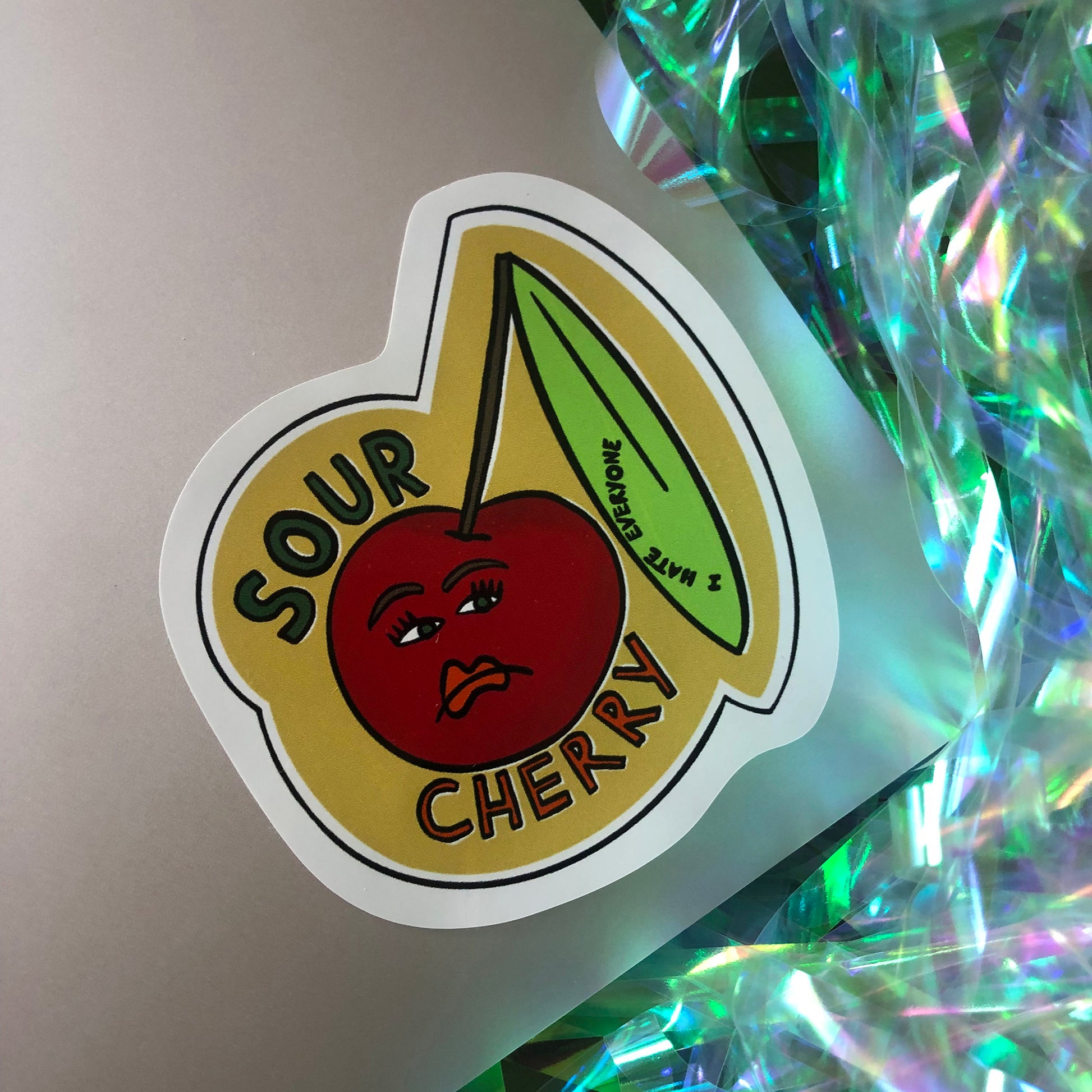 Image shows a vinyl sticker featuring an illustration of an unhappy looking cherry and the wording 'Sour Cherry'