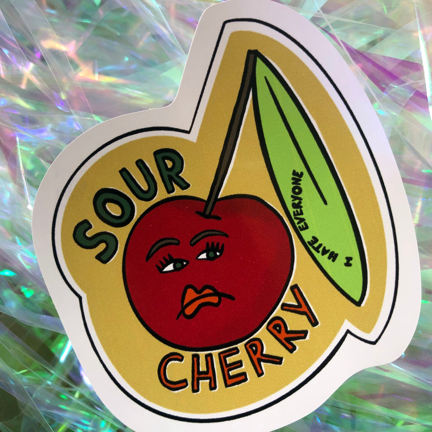 Image shows a vinyl sticker featuring an illustration of an unhappy looking cherry and the wording 'Sour Cherry'