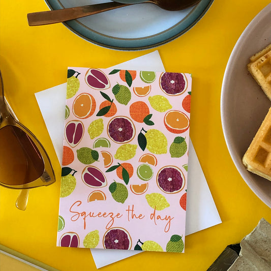 Image shows an everyday greetings card that says 'squeeze the day' and features a fun pattern of lemons, oranges, tangerines and grapefruit