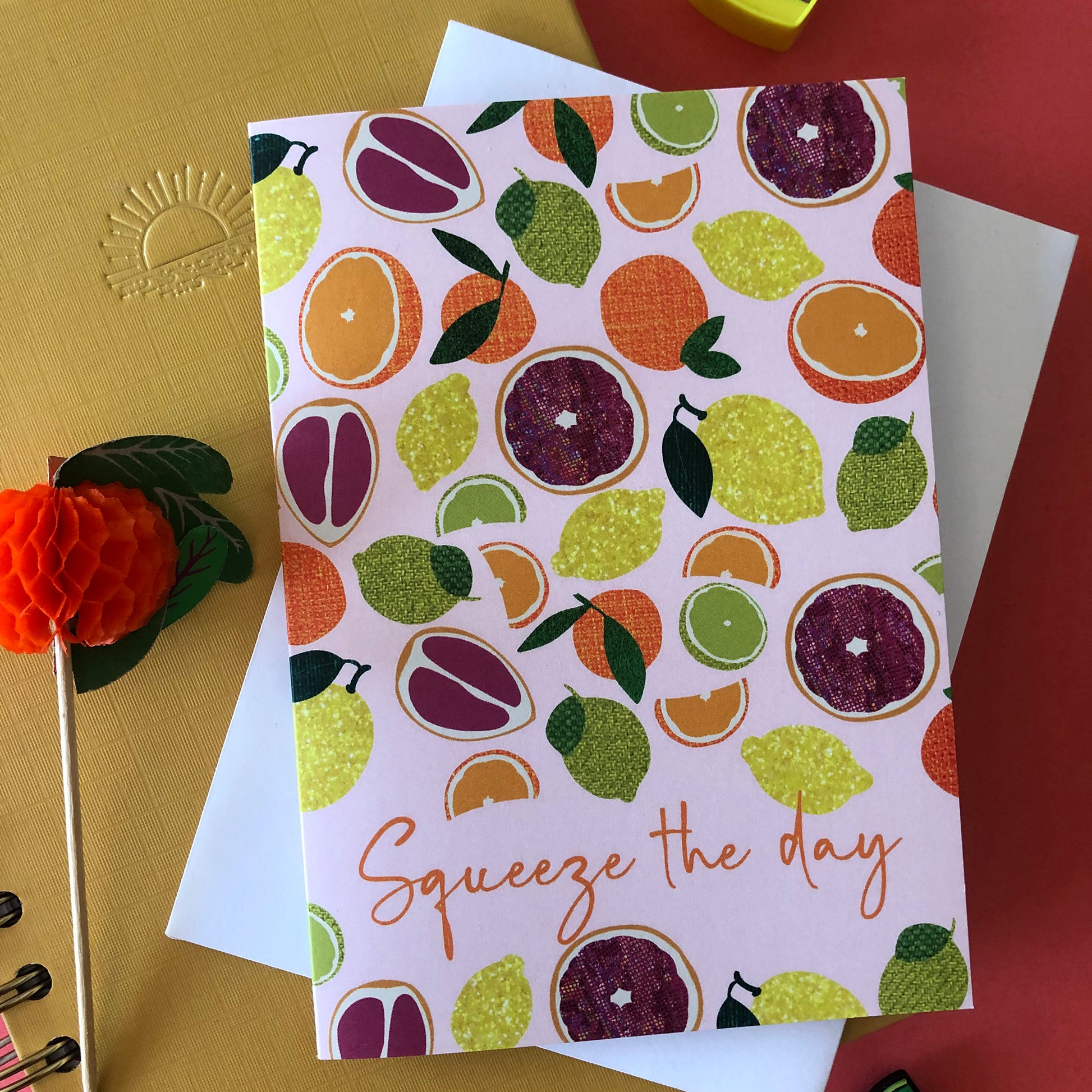 Image shows an everyday greetings card that says 'squeeze the day' and features a fun pattern of lemons, oranges, tangerines and grapefruit