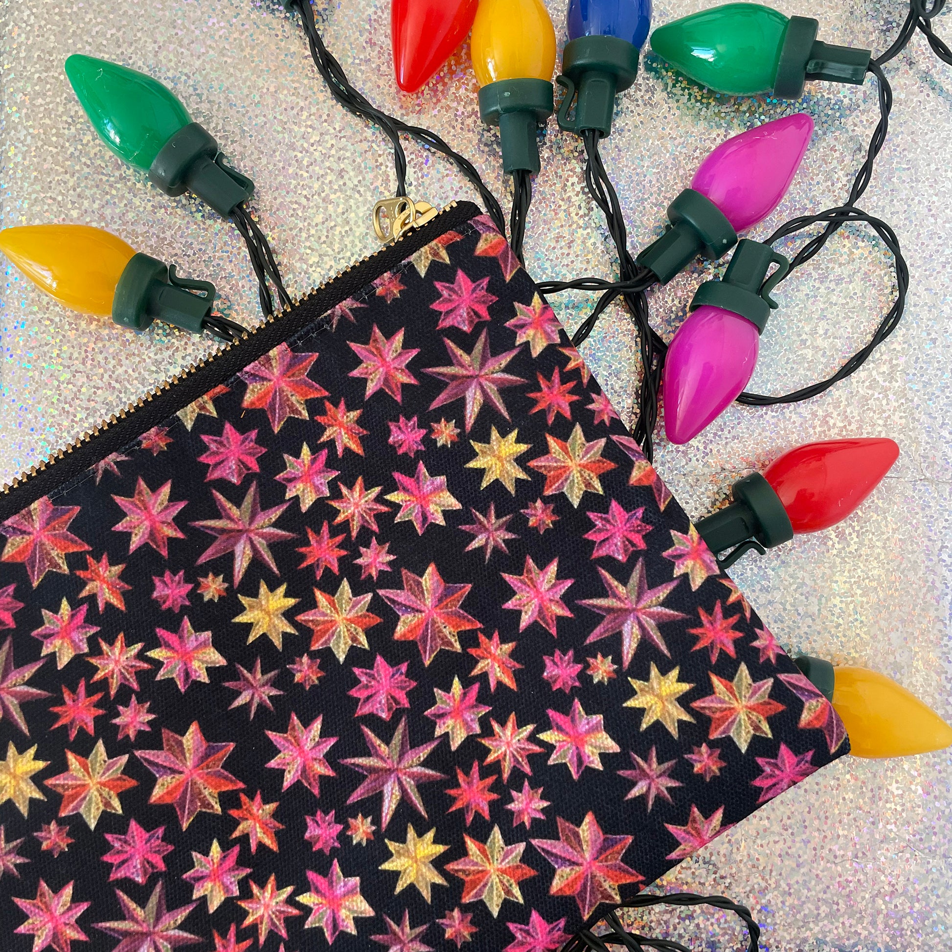 Image shows a black zip pouch with a bright pink, orange and gold starlight lantern design.