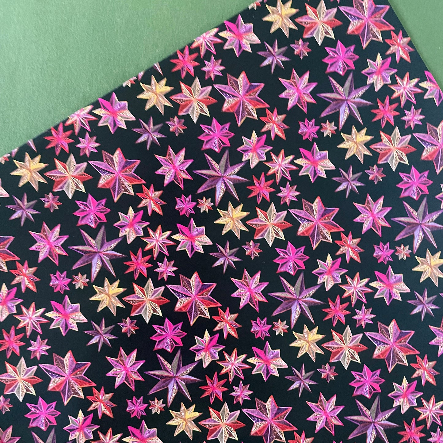 Image shows a gift wrap sheet in black with a bright pink and gold folk art star pattern.