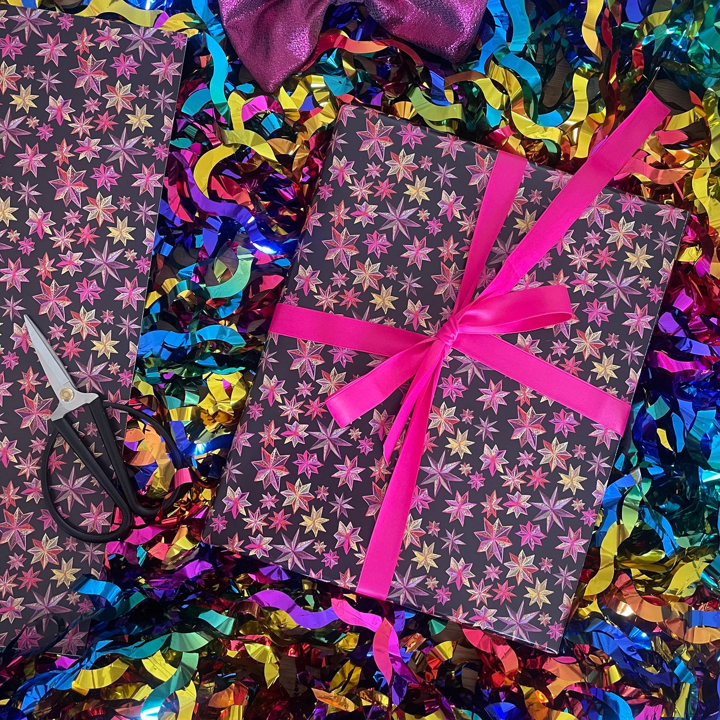 Image shows a wrapped gift in black paper with a bright pink and gold folk art star pattern.