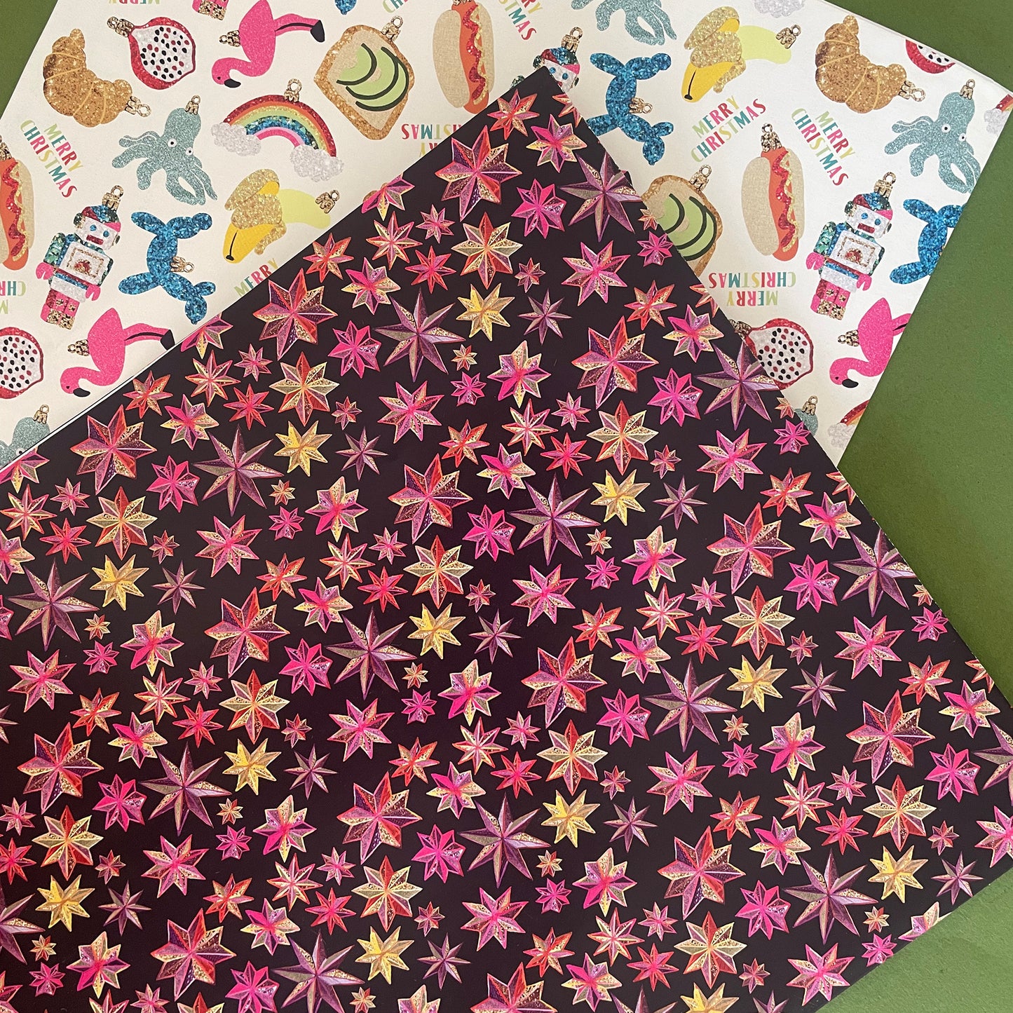 Image shows a gift wrap sheet in black with a bright pink and gold folk art star pattern.