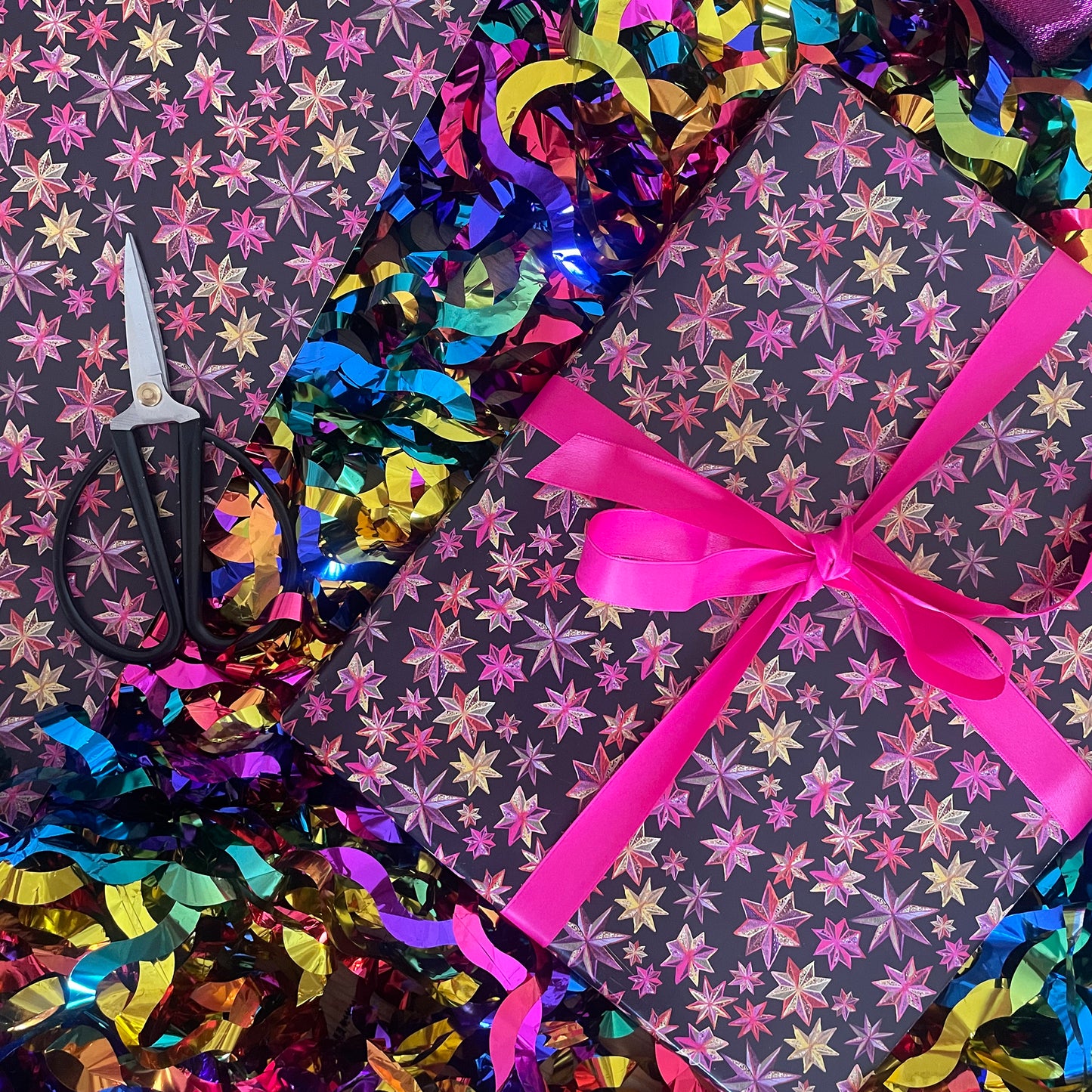 Image shows a wrapped gift in black paper with a bright pink and gold folk art star pattern.