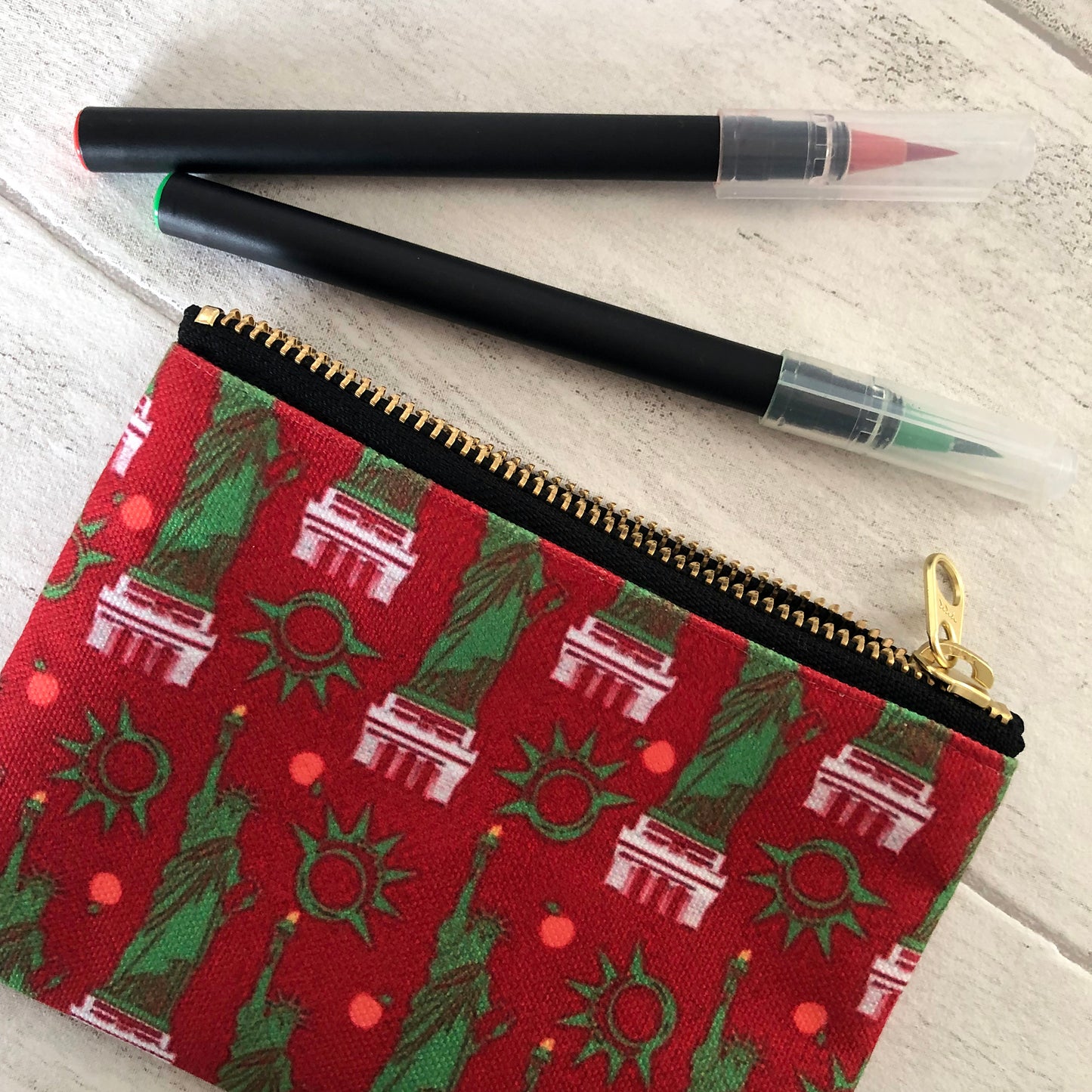 Image shows a handy zip pouch in a bold red colour with a statue of liberty pattern in green and white.