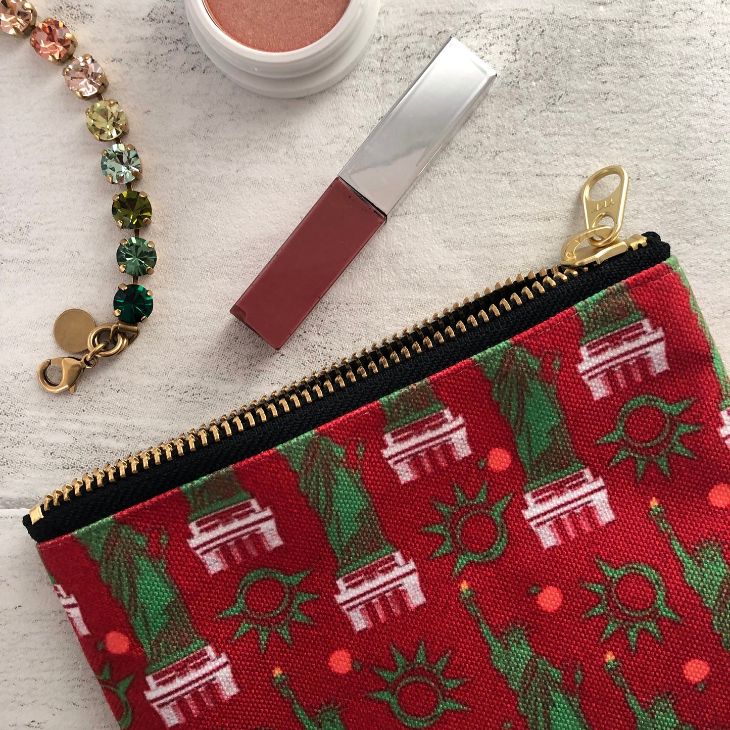 Image shows a handy zip pouch in a bold red colour with a statue of liberty pattern in green and white.