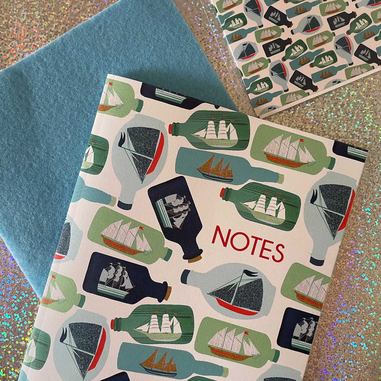 Image of a ships in bottles print A5 size notebook in a cream colour with blue and green bottles.