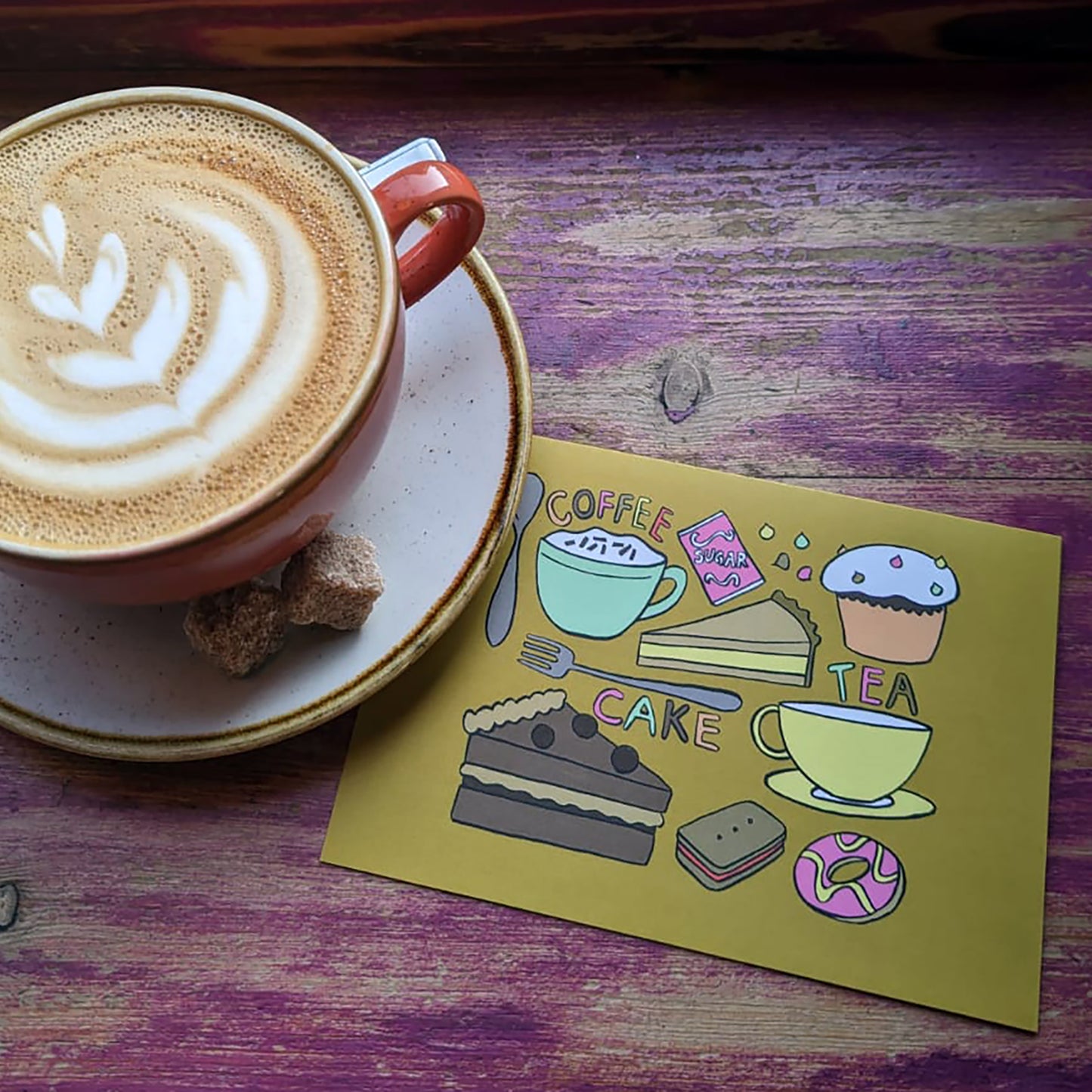Image shows an ochre coloured illustrated notecard featuring delicious tea time treats.