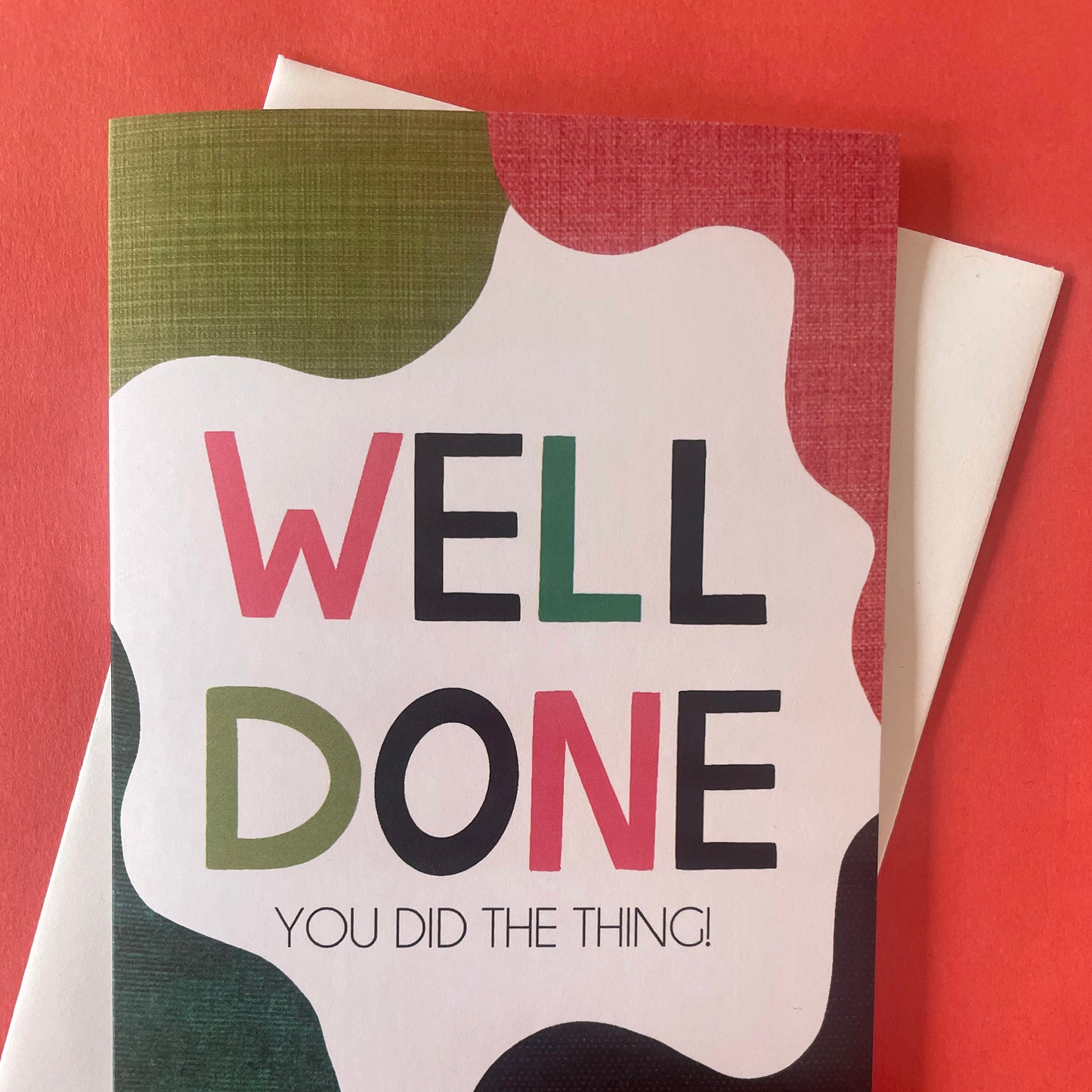 Image shows a bright greetings card with colourful, abstract shapes around the edge and the wording "Well Done you did the thing"