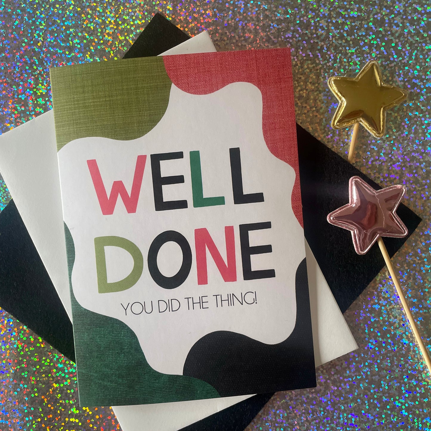 Image shows a bright greetings card with colourful, abstract shapes around the edge and the wording "Well Done you did the thing"