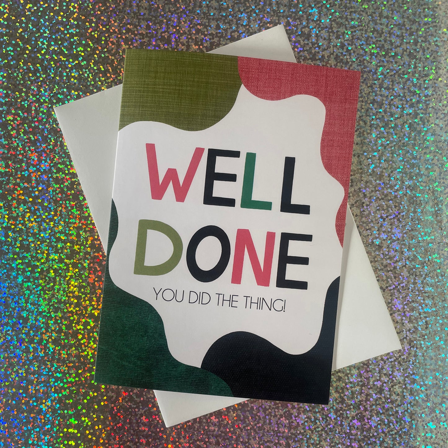 Image shows a bright greetings card with colourful, abstract shapes around the edge and the wording "Well Done you did the thing"